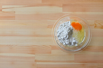 Raw eggs and flour in glass bowls are on the wooden board in the kitchen.