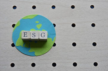 There is the earth and word cube formed "ESG" which are placed on a puching board. © hogehoge511