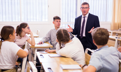 Obraz premium Smiling male lecturer explaining new theme and helping teenage students during class