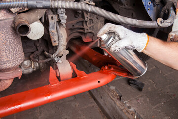 A car mechanic cleans and maintains the engine chassis of an old car against corrosion and protects it with a preparation