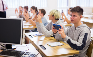 Group of focused teenagers using phones at class in auditorium