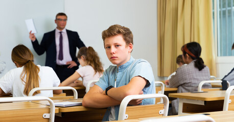 Fototapeta na wymiar Sad upset teenage schoolboy sitting separately in classroom during lesson in college
