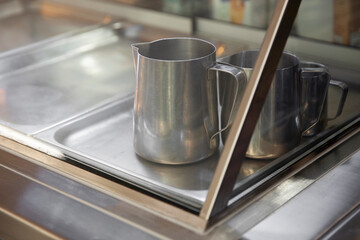 Stainless steel barista jugs in empty bain-marie.