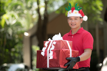 Asian delivery man in red uniform and Christmas hat delivering present and gift boxes to recipient...