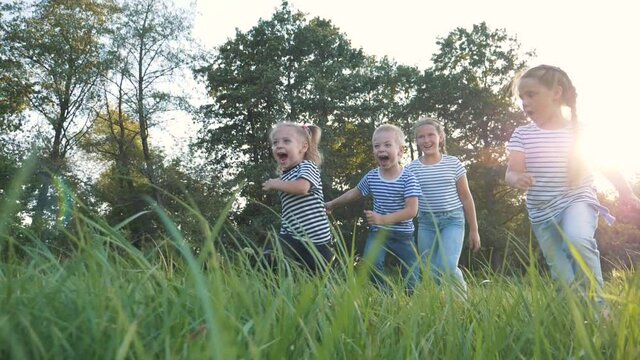 Happy family of children has fun in the park. Children flee the green lawn in droves. Kids play fun at sunset in the park. Teamwork, playing girls and a boy.
