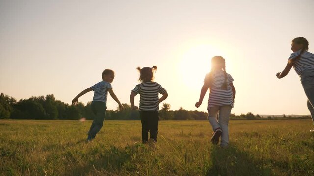 A happy family of children have fun in the park at sunset. Silhouette of fleeing children. Children flee the green lawn in droves. Kids in the park play fun, laugh. Teamwork, playing girls and a boy.