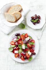 Simple salad with cherry tomatoes, feta cheese, kalamata olives, red pepper and fresh herbs. Bright wooden background. Top view. 