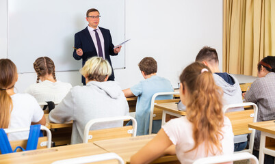 Fototapeta na wymiar Portrait of adult male teacher conducting lesson for teenage schoolchildren listening attentively to him