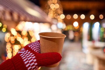 Christmas Market in European small city. Hand holding a cup of mulled wine with blurred background of winter wonderland, a