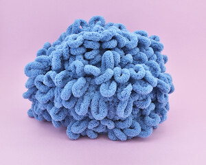 Skein of thick blue puffy yarn for knitting on a pink background