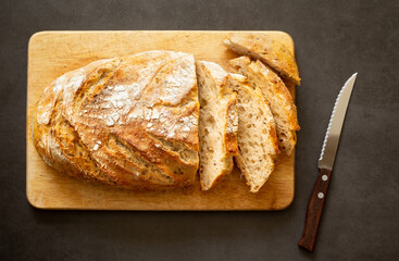 Homemade bread cut into slices on a wooden plank with a knife