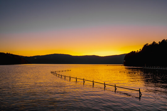 The view of sticks are embroidered in the water arranged in a row in the evening. The sun is setting, making the sky twilight color. There are mountains behind. Idea for natural light with copy space.
