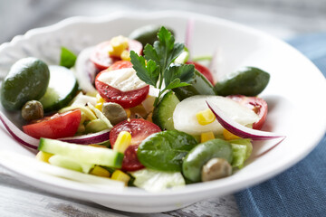 Healthy Salad with Green Olives, Baby Spinach, Cucumber, Cherry Tomatoes and Capers. Bright wooden background. Close up. 