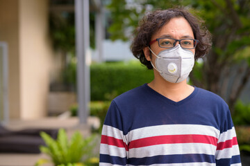 Japanese man with curly hair wearing mask and thinking in the rooftop garden