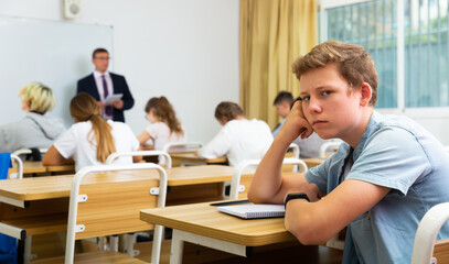 Sad boy sitting at desk in a school class