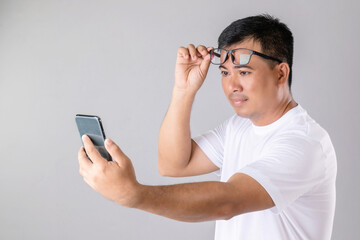 Short or long sighted concept : Man weraing eyeglasses and trying to look clearly on smarthphone in studio shot on grey