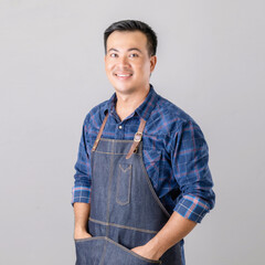 Asian man in barista uniform standing in studio isolated on grey background