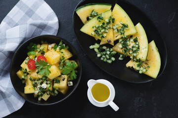 Yellow watermelon and herbed cucumber salad, above view over black stone background, horizontal shot