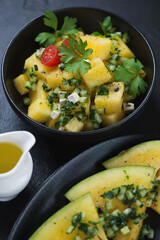 Salad with yellow watermelon cubes, herbed cucumber and fresh parsley served in a black bowl, vertical shot, closeup
