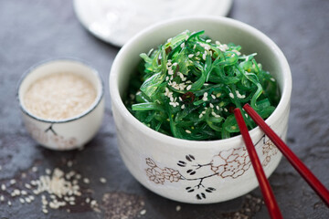 Chuka salad topped with sesame seeds and served in a white bowl, studio shot on a brown stone surface
