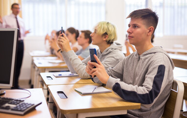 Group of teenage students using smartphones in classroom at school