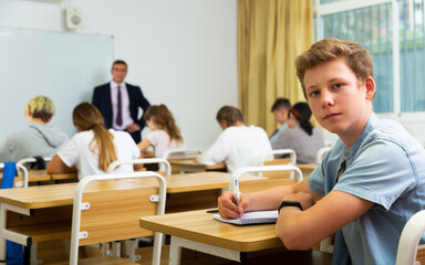 Fototapeta premium Portrait of confident teenage student sitting on lesson in classroom, looking at camera