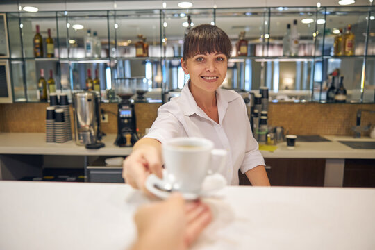 Cheeful pretty barmaid serving client with hot drink