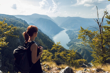 Female hiker with backpack standing on top of the mountain enjoying the view during the day.