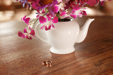 Wedding rings on woodn table near vase wth purple orchid flowers