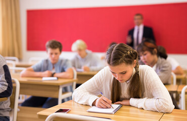 Fototapeta na wymiar Portrait of positive teenage female pupil sitting at desk studying in classroom