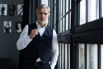 Fototapeta premium Success concept. Stylish mature bearded man in elegant suit standing near the window