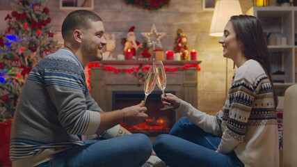 Couple having a conversation and drinking champagne while celebrating christmas in front of fireplace.