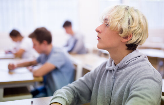 Smart teenager studying in classroom, listening to lecturer and writing in notebook..