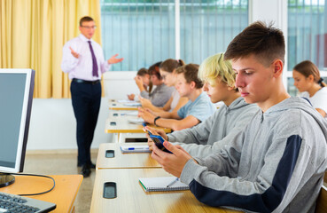 Side view of student group working with mobile phones in school class