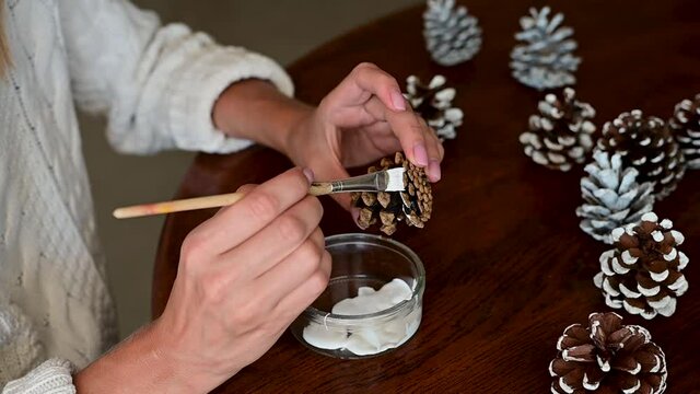 Female hands decorate pine cones with white paint. Christmas Crafts. Close-up.