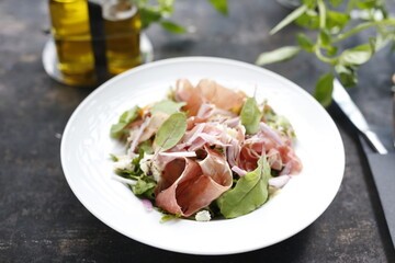 Salad with Parma ham, tomatoes, yellow beetroot, and vinaigrette sauce.
Appetizing dish served on a white plate. culinary photography.
