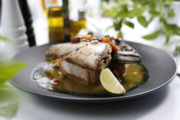 Roasted mackerel. Whole fish served with garlic, olives, and lemon.
Appetizing dish served on a black plate .Culinary photography, food photography.