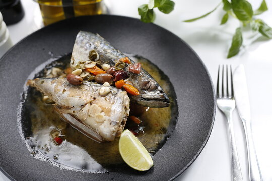 Roasted mackerel. Whole fish served with garlic, olives, and lemon.
Appetizing dish served on a black plate .Culinary photography, food photography.