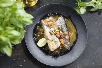 Roasted mackerel. Whole fish served with garlic, olives, and lemon.
Appetizing dish served on a black plate .Culinary photography, food photography.
