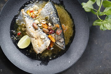 Roasted mackerel. Whole fish served with garlic, olives, and lemon.
Appetizing dish served on a black plate .Culinary photography, food photography.