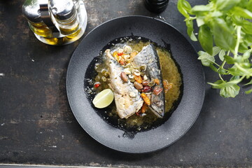 Roasted mackerel. Whole fish served with garlic, olives, and lemon.
Appetizing dish served on a black plate .Culinary photography, food photography.
