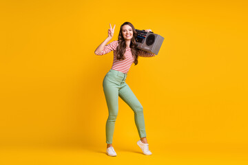 Fototapeta na wymiar Full length body size photo of girl listening to retro boombox showing v-sign gesture isolated on vivid yellow color background