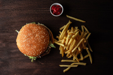 close-up of a hamburger and a pile of French fries on a wooden background - obrazy, fototapety, plakaty