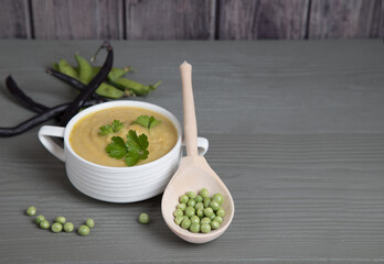 Soup-mashed peas and beans in a white Cup on a gray wooden background, a wooden spoon with peas lies next to it . Place for a copy space
