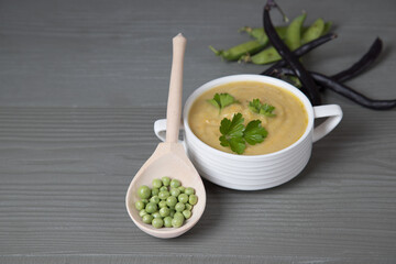 Soup-mashed peas and beans in a white Cup on a gray wooden background, a wooden spoon with peas lies next to it . Place for a copy space