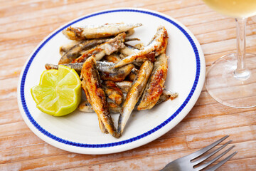 Tasty fried anchovies served with lemon at plate, Spanish cuisine