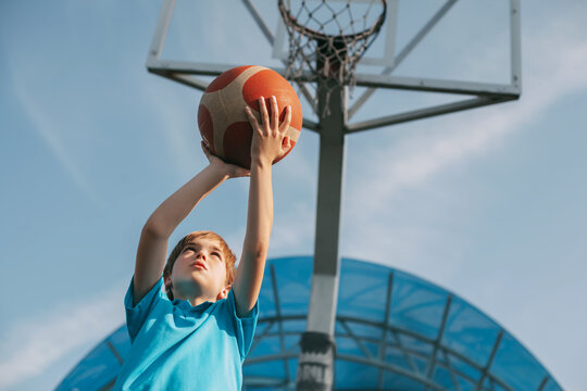 A boy in a sports uniform throws a ball into a basketball basket. A child plays basketball. Sports, lifestyle, place for text