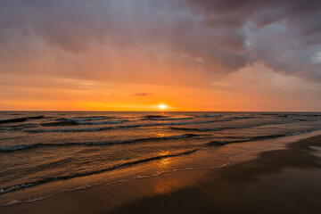 Fototapeta na wymiar Waves at a beach sunrise with dramatic sky