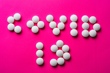 inscription COVID 19 from many white pills on a pink background. accept gifts concept. Cardiology or love concept