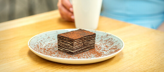 Piece of chocolate cake on plate with cup of coffee on the table in dessert cafe
